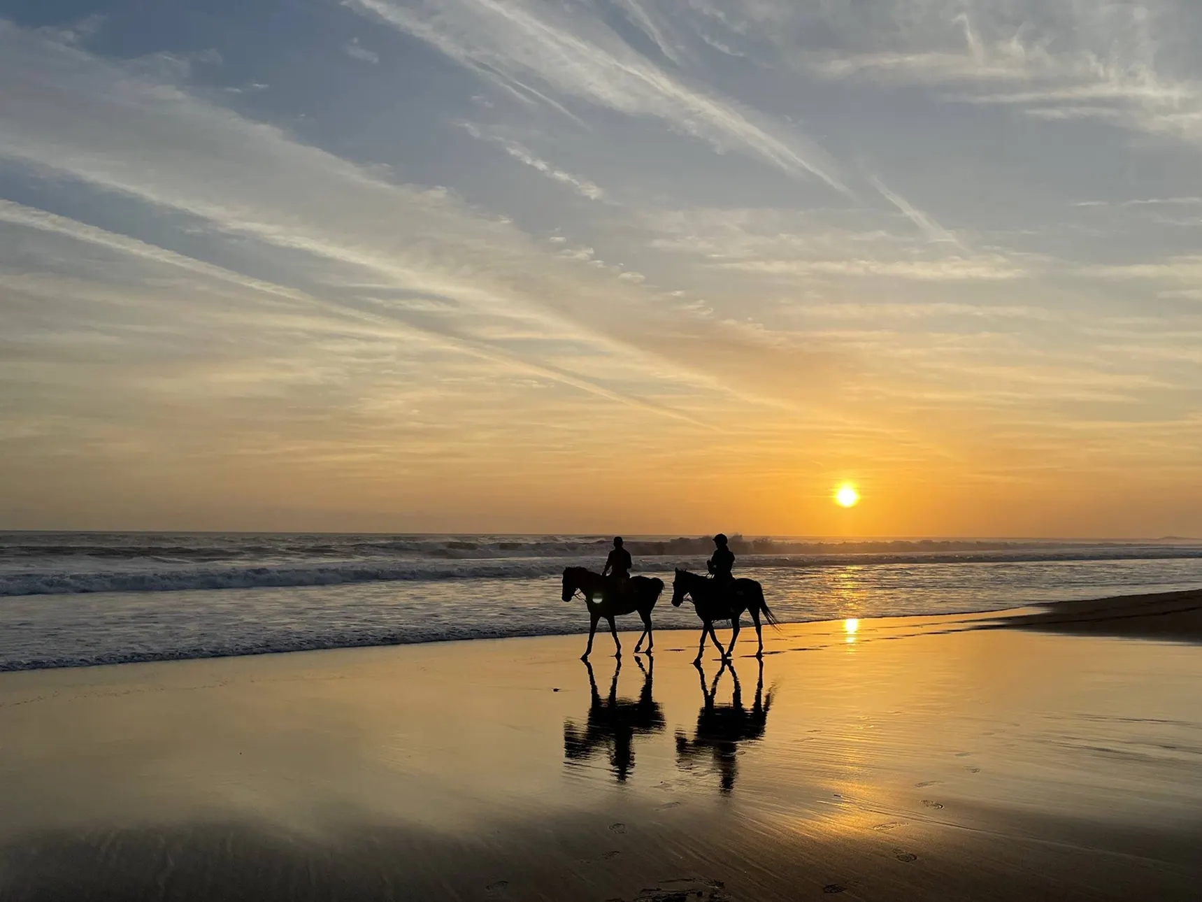 夕暮れの浜辺を馬で駆ける2人